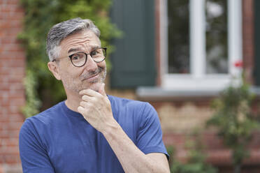 Mann mit Brille und Hand am Kinn vor einem Haus - RORF03138