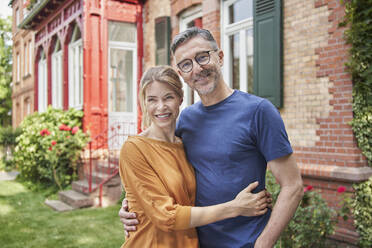 Smiling woman embracing man in front of house - RORF03142