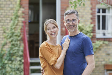 Smiling man embracing happy woman in front of house - RORF03187