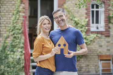 Glückliches Paar hält Holzhausmodell im Garten - RORF03192