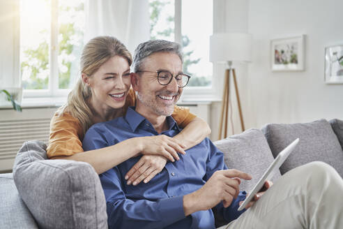 Happy woman embracing man using tablet PC on sofa at home - RORF03202