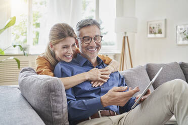 Happy man showing tablet PC with woman at home - RORF03204