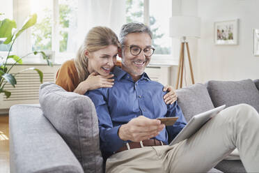Happy woman with arm around man with credit card online shopping through table PC on sofa - RORF03205