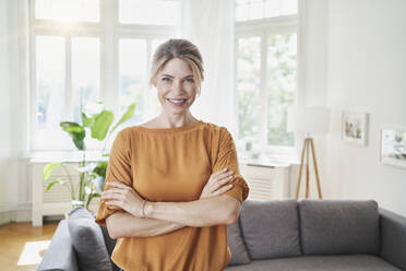 Smiling woman with arms crossed in living room at home - RORF03216