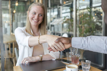 Glückliche Geschäftsfrau schüttelt die Hände mit einem Kollegen in einem Cafe - TAMF03610