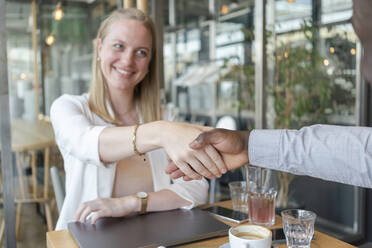 Happy businesswoman shaking hands with colleague in cafe - TAMF03610