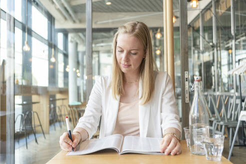 Junge Geschäftsfrau, die im Café mit einem Stift in einer Zeitschrift markiert - TAMF03612