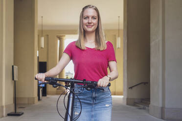 Lächelnde Frau steht mit Fahrrad vor einem Gebäude - TAMF03630
