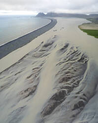 Luftaufnahme einer Wasserformation an einer Flussmündung und des Strandes Fjorur mit einem Berg im Hintergrund, Island. - AAEF17017