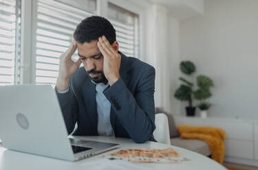 A depressed businessman man counting euro money working on computer at office desk, inflation concept. - HPIF00950