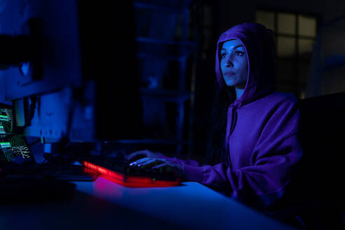 Eine junge Frau hackt sich nachts in einem dunklen Raum in einen Computer ein, Cyberwar-Konzept. - HPIF00981