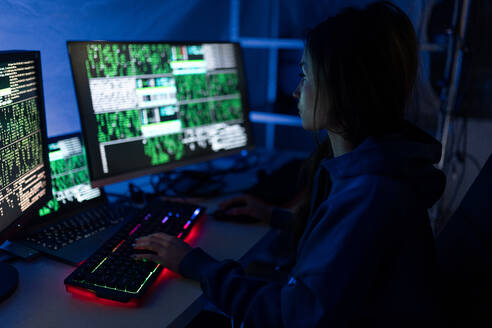 Eine junge Frau hackt sich nachts in einem dunklen Raum in einen Computer ein, Cyberwar-Konzept. - HPIF00983