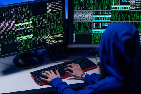 Eine Rückansicht eines vermummten Hackers am Computer in einem dunklen Raum bei Nacht, Cyberwar-Konzept. - HPIF00993