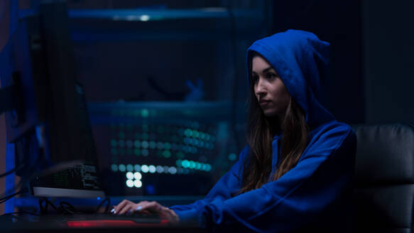Eine junge Frau hackt sich nachts in einem dunklen Raum in einen Computer ein, Cyberwar-Konzept. - HPIF00994