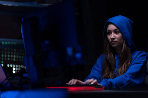 Eine junge Frau hackt sich nachts in einem dunklen Raum in einen Computer ein, Cyberwar-Konzept. - HPIF00995