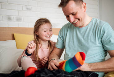 Ein Vater zieht seiner kleinen Tochter mit Down-Syndrom verschiedene Socken an, wenn sie zu Hause im Bett sitzt. - HPIF01003