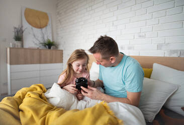 Ein Vater stellt den Wecker, während seine kleine Tochter mit Down-Syndrom zu Hause im Bett liegt. - HPIF01009