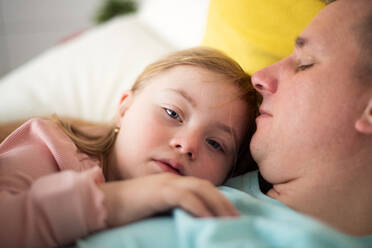 Ein Vater ruht sich mit seiner kleinen Tochter mit Down-Syndrom zu Hause im Bett aus. - HPIF01013