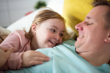 A father with hugging his little daughter with Down syndrome on bed at home. - HPIF01014