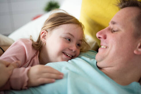 Ein Vater, der seine kleine Tochter mit Down-Syndrom zu Hause im Bett umarmt. - HPIF01014