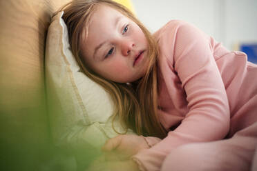 Ein trauriges kleines Mädchen mit Down-Syndrom liegt zu Hause im Bett. - HPIF01016