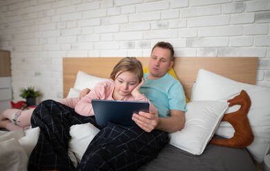 A father and his little daughter with Down syndrome lying on bed and using tablet at home. - HPIF01017