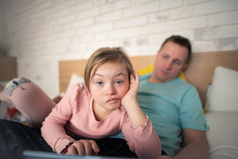 Ein Vater ruht sich mit seiner kleinen Tochter mit Down-Syndrom zu Hause im Bett aus. - HPIF01018