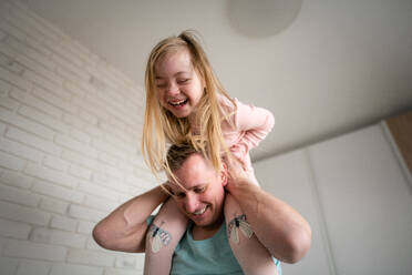 Ein Vater hält seine kleine Tochter mit Down-Syndrom zu Hause auf den Schultern. - HPIF01023