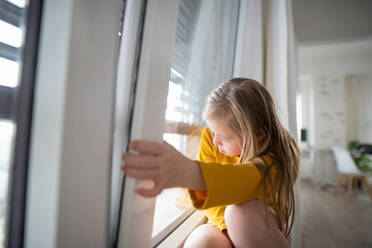 Ein neugieriges kleines Mädchen mit Down-Syndrom, das durch ein Fenster zu Hause schaut. - HPIF01032