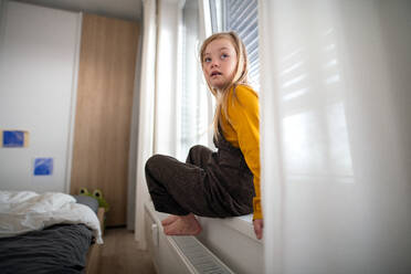 Ein trauriges kleines Mädchen mit Down-Syndrom sitzt zu Hause am Fenster. - HPIF01038