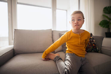 Ein trauriges kleines Mädchen mit Down-Syndrom sitzt zu Hause auf dem Sofa. - HPIF01043