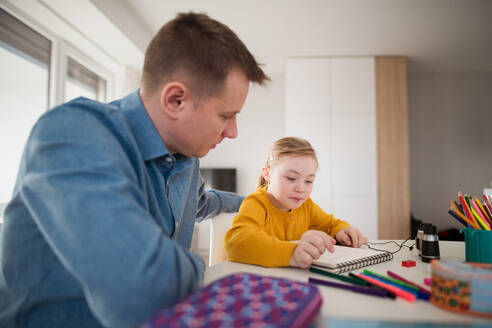 Ein Vater mit seiner kleinen Tochter mit Down-Syndrom beim Lernen zu Hause. - HPIF01047
