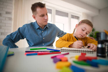 Ein Vater mit seiner kleinen Tochter mit Down-Syndrom beim Lernen zu Hause. - HPIF01049