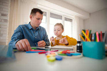 Ein Vater mit seiner kleinen Tochter mit Down-Syndrom beim Lernen zu Hause. - HPIF01050