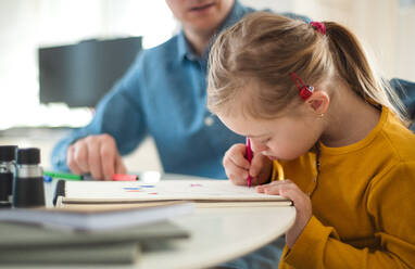 Ein Vater mit seiner kleinen Tochter mit Down-Syndrom beim Lernen zu Hause. - HPIF01053