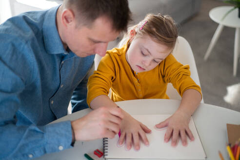 Ein Vater mit seiner kleinen Tochter mit Down-Syndrom beim Lernen zu Hause. - HPIF01057