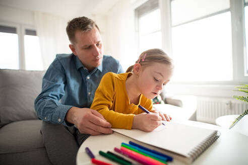 Ein Vater mit seiner kleinen Tochter mit Down-Syndrom beim Lernen zu Hause. - HPIF01062
