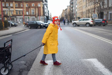 Ein kleines Mädchen mit Down-Syndrom überquert die Straße und zieht den Wagen. - HPIF01082