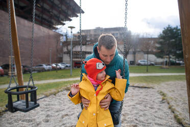 Ein Vater schiebt seine kleine Tochter mit Down-Syndrom auf einer Schaukel im Freien in einer Spielhalle. - HPIF01090