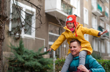 Ein Vater bringt seine kleine Tochter mit Down-Syndrom im Huckepack zur Schule, draußen auf der Straße. - HPIF01094