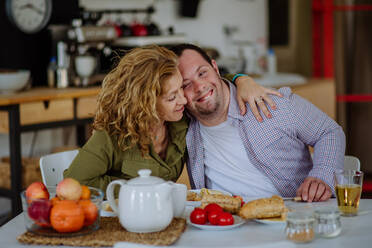 Ein Porträt eines glücklichen Mannes mit Down-Syndrom und seiner Mutter beim gemeinsamen Frühstück zu Hause. - HPIF01106