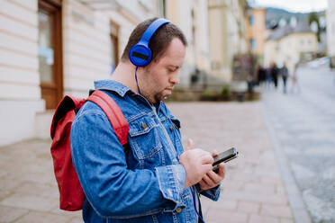 Ein glücklicher junger Mann mit Down-Syndrom, der beim Gehen auf der Straße Musik hört. - HPIF01112