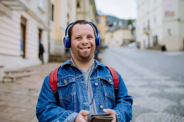 Ein glücklicher junger Mann mit Down-Syndrom, der beim Gehen auf der Straße Musik hört. - HPIF01113
