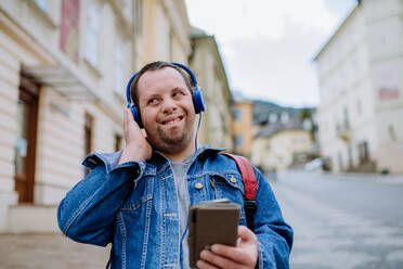 Ein glücklicher junger Mann mit Down-Syndrom, der beim Gehen auf der Straße Musik hört. - HPIF01114