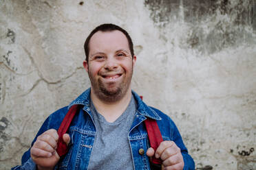 Porträt eines glücklichen jungen Mannes mit Down-Syndrom mit Rucksack auf der Straße, lächelnd. - HPIF01117