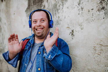 Nahaufnahme eines glücklichen jungen Mannes mit Down-Syndrom, der beim Gehen auf der Straße Musik hört. - HPIF01119