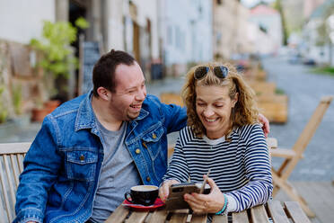 A portrait of happy young man with Down syndrome with his mother sitting in cafe outdoors and talking. - HPIF01123