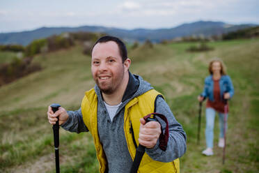 Ein Porträt eines glücklichen jungen Mannes mit Down-Syndrom und seiner Mutter, die gemeinsam in der Natur wandern. - HPIF01125