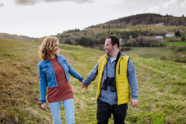 Ein glücklicher junger Mann mit Down-Syndrom und seine Mutter gehen in der Natur spazieren und halten sich gegenseitig an der Hand. - HPIF01134