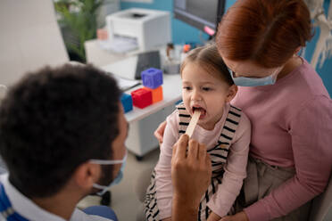 Ein junger männlicher Arzt untersucht in seiner Praxis den Hals eines kleinen Mädchens. - HPIF01147